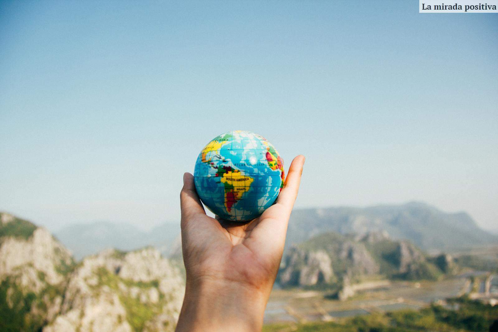 Person Holding World Globe Facing Mountain