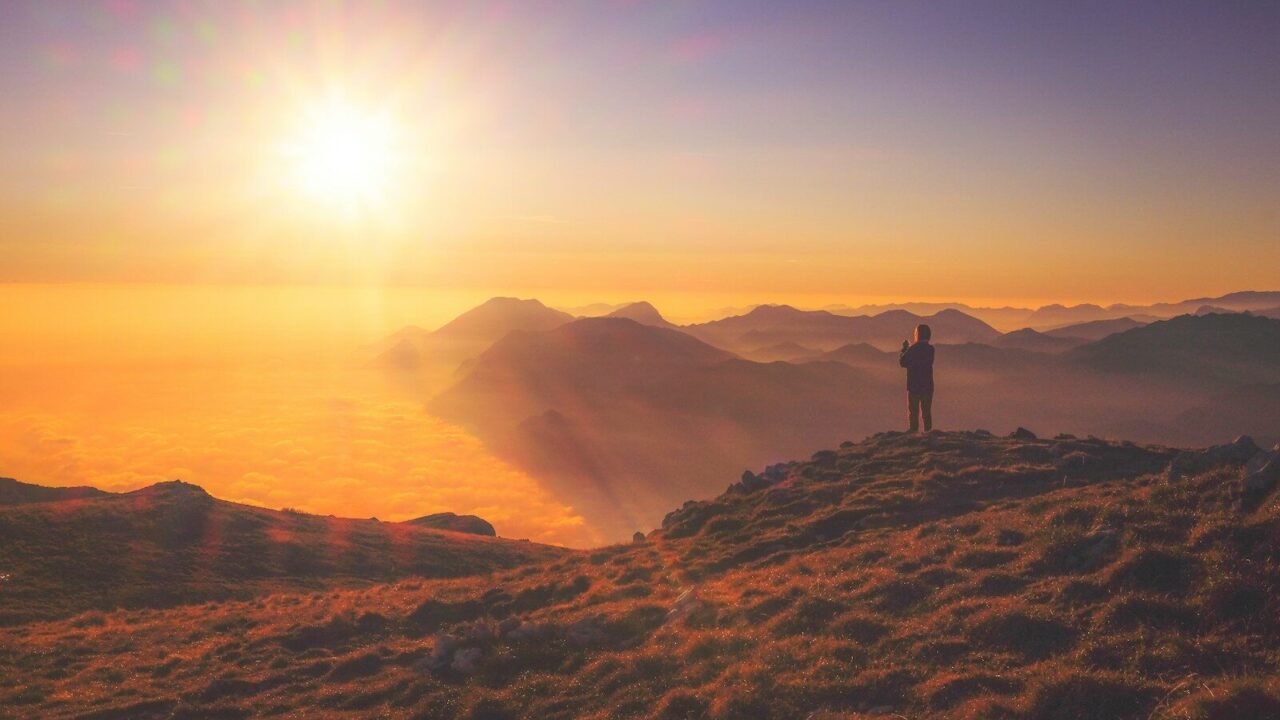 Persona contemplando el amanecer sobre un mar de nubes, imagen de pensamiento positivo
