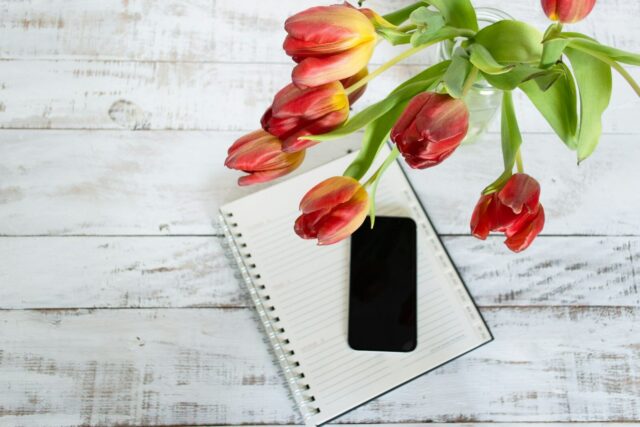 Cuaderno, móvil y tulipanes sobre una mesa blanca de trabajo