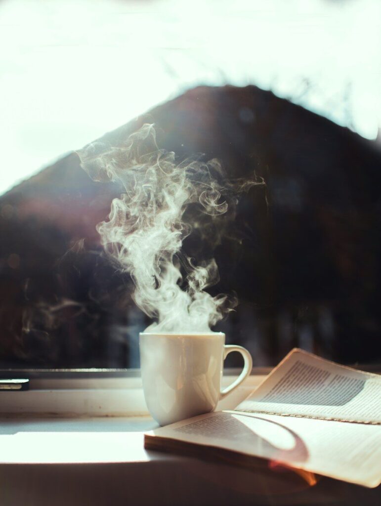Taza de café humeante junto a un libro abierto, momento para practicar ejercicios de pensamiento positivo